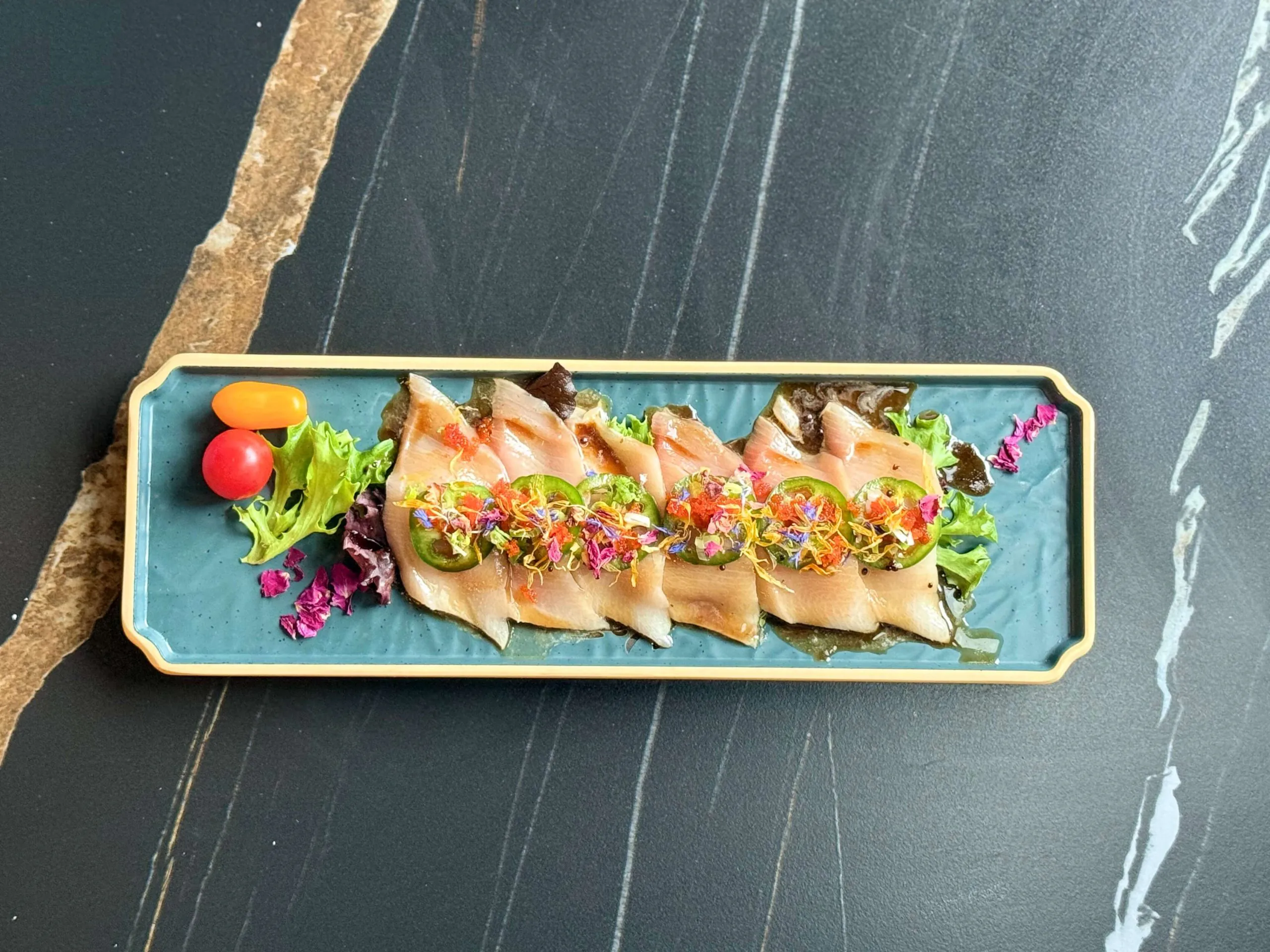 Yellow tail sashimi slices topped with jalapenos and colorful seasonings